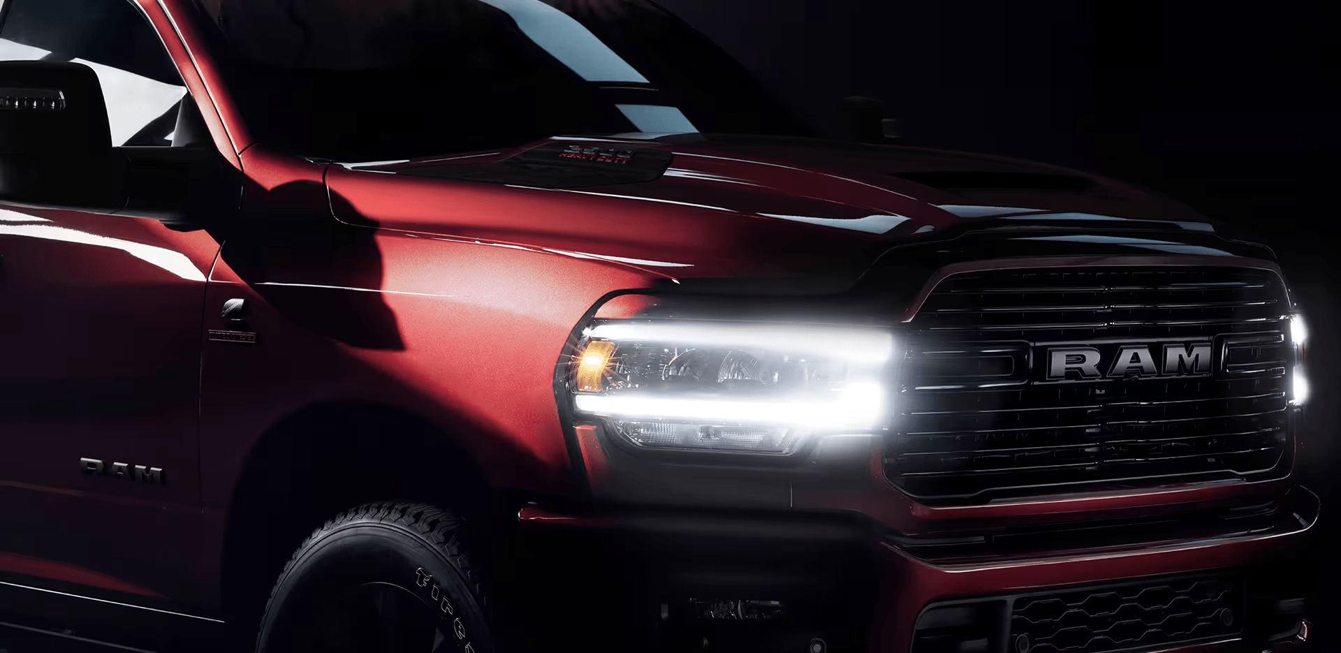 A close-up of the passenger-side front end of a red RAM 2500 Laramie with its Daytime Running Lamps and cornering lamps on.